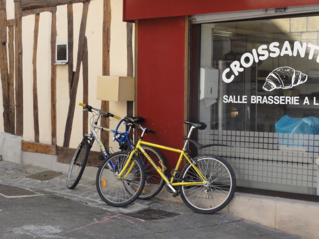 Zwei Fahrräder nebeneinander auf einem Gehweg vor einem Laden mit einer Glaswand, auf der Text und ein Objekt zu sehen sind.