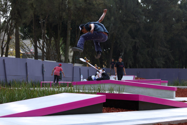 Ein Skateboarder zeigt einen Sprung auf einer Rampe, umgeben von Zuschauern und verstreuten Gegenständen.