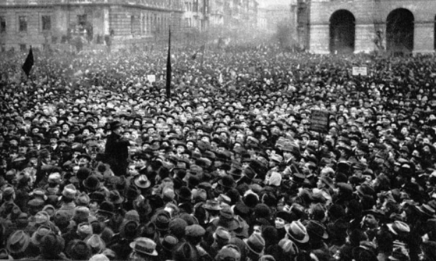 Ein Schwarz-Weiß-Bild einer großen Menschenmenge bei einer Demonstration, mit einer Person in der Mitte, die eine Fahne und ein Schild hält, wahrscheinlich eine Suffragetten-Veranstaltung.