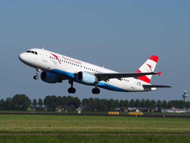 Austrian Airlines Airbus A320-200 startet von Frankfurt Airport, mit grünem Gras, Bäumen, Gebäuden und einer Kontrollturm im Hintergrund.