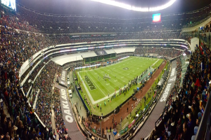 Ein großes Stadion voller Zuschauer, die ein Fußballspiel sehen, mit Spielern und Gegenständen auf dem Feld, beleuchteten Tafeln, Geländern, Bildschirmen und Deckenlampen.
