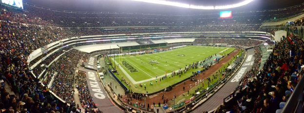 Ein großes Stadion voller Zuschauer, die ein Fußballspiel sehen, mit Spielern und Gegenständen auf dem Feld, beleuchteten Tafeln, Geländern, Bildschirmen und Deckenlampen.