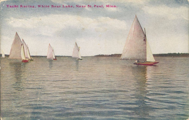 Gruppe von Segelbooten bei einem Regatta auf dem White Bear Lake in der Nähe von St. Paul, Minnesota, mit Bäumen im Hintergrund und einem klaren blauen Himmel.