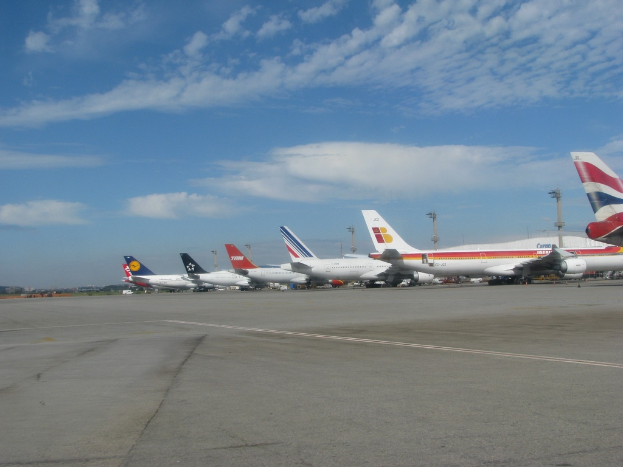 Mehrere Flugzeuge sind auf einer Rollbahn mit Polen und Kabeln in der Nähe aufgereiht, unter einem bewölktem Himmel.