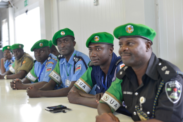 Gruppe von Polizeibeamten, die an einem Tisch mit Mobiltelefonen und anderen Gegenständen während einer Schulung in einem Raum mit Fenstern und Deckenbeleuchtung sitzen.