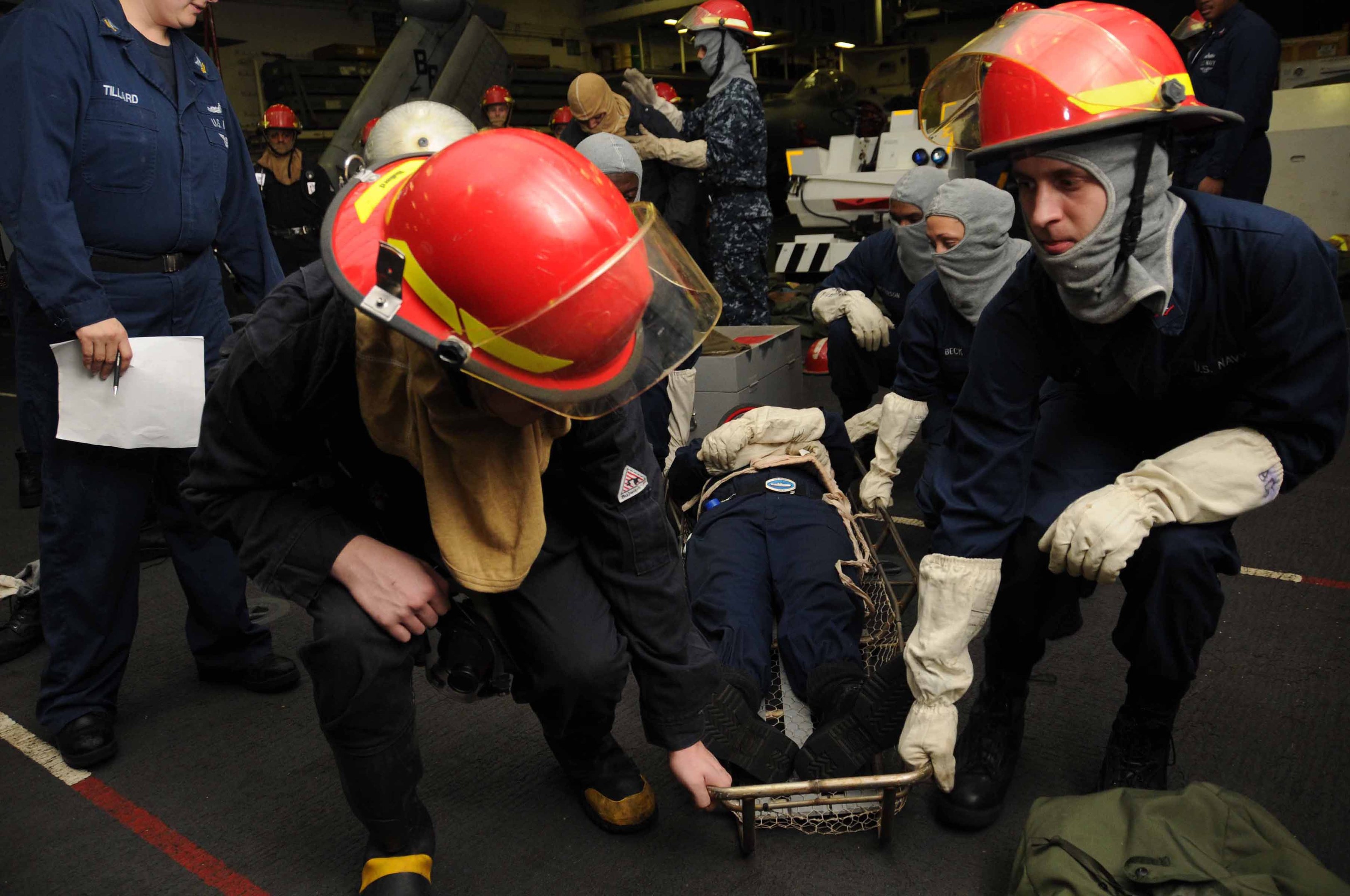 Rettungsteam auf einem Schiffdeck, das einer Person auf einer Bahre hilft, wobei ein Mitglied Dokumente hält und ein weiteres Ausrüstung trägt, umgeben von verstreuter Ausrüstung und Deckenbeleuchtung.