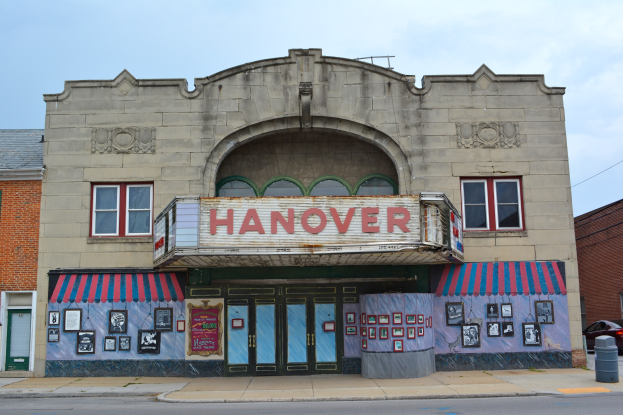 Außenansicht des Hanover Theatre in St. Louis, Missouri, mit Glasfenstern, einem Namenbrett, Fotoeinrahmen, einem Mülleimer, einem Auto auf der Straße und einem bewölkten Himmel.