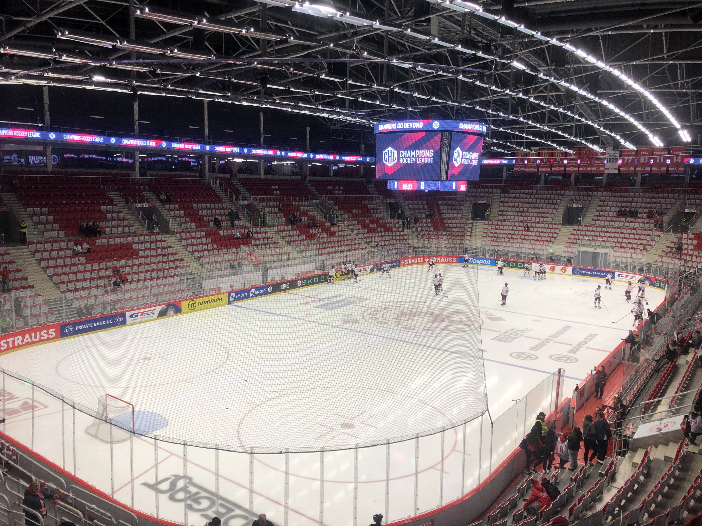 Ein Eishockeyspiel in einer großen Arena mit Zuschauern auf den Sitzplätzen und Stehplätzen, einem Zaun um die Eisfläche, einem Display mit der Aufschrift "St. Louis Blues vs Detroit Red Wings", Metallrahmen und einer Decke mit Deckenleuchten.
