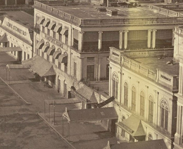 Altes Schwarz-Weiß-Foto einer Stadtstraße mit Gebäuden, Fenstern, Säulen, Namensschildern, Schuppen und Masten.