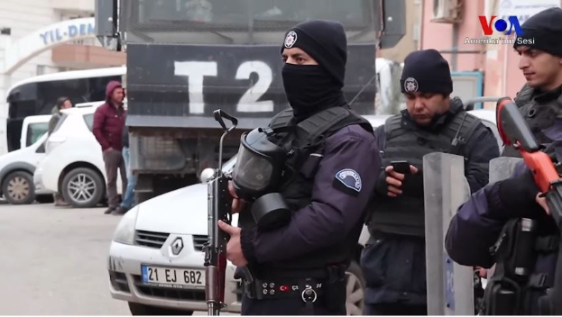 Eine Gruppe von Polizisten in Uniform steht zusammen auf einer Straße während einer Anti-Regierungsdemo in Ankara, Türkei, mit Waffen in der Hand, während Fahrzeuge, Menschen, Gebäude und Texttafeln im Hintergrund zu sehen sind.