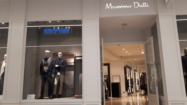 Innenansicht des Massimo Dutti-Geschäfts in Mailand, Italien, das modernos Mode-Kleidung tragende Schaufensterpuppen, beleuchtete Deckeninstallationen, Informationsschilder und sichtbaren Boden zeigt.