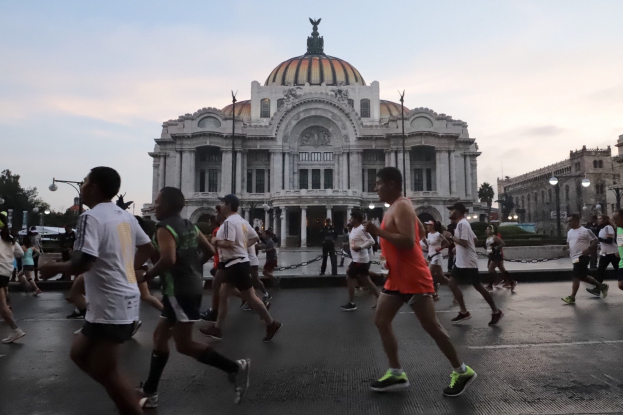 Gruppe von Läufern vor einem großen Gebäude während eines Marathons, mit Straßenlaternen, Bäumen und einem bewölkten Himmel im Hintergrund.