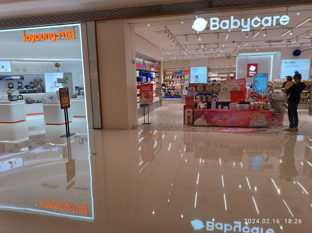 Babybedarfsgeschäft im Einkaufszentrum Mall of Asia mit Regalen voller Artikel, Schildern, einem Display, Deckenleuchten und Menschen, die Spielzeuge und Gegenstände durchstöbern.
