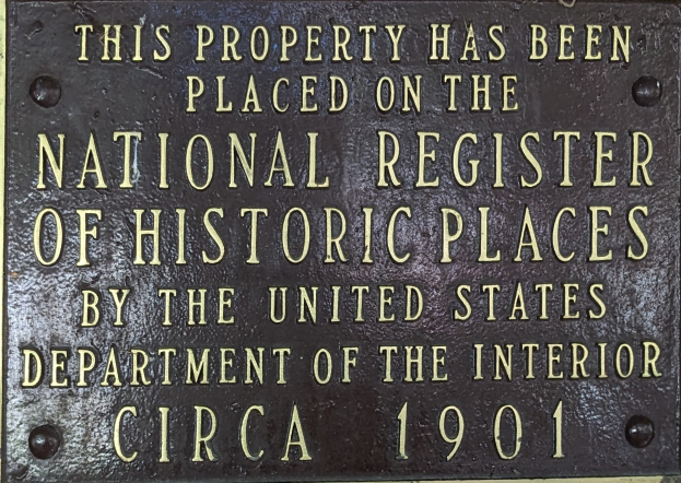 Eine Metalltafel an einem Gebäude trägt die Inschrift "Dieses Gebäude steht unter Denkmalschutz".