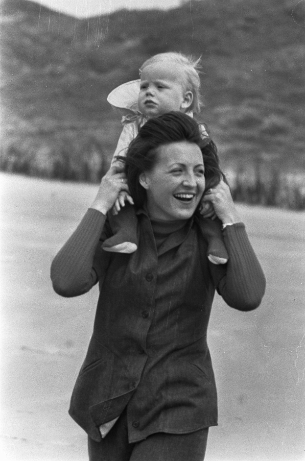 Eine Frau mit warmem Lachen h├Ąlt ein Baby in den Armen, mit einem leicht unscharfen Hintergrund, der einen traumhaften, nostalgischen Effekt erstellt.