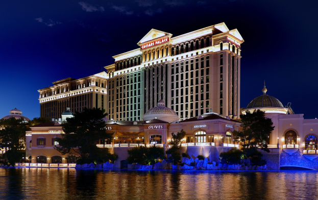 Außenansicht des Caesars Palace Hotels und Casinos in Las Vegas, Nevada, mit Wasser im Vordergrund und Gebäuden, Bäumen, Lichtern und einem bewölkten Himmel im Hintergrund.