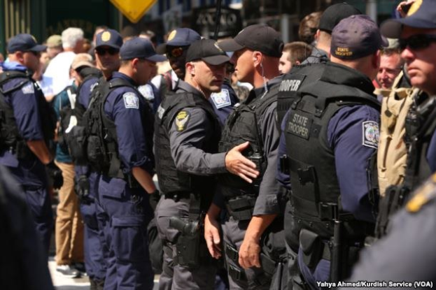Eine Gruppe von Polizisten in Uniform, die auf einer Straße in Formation stehen, einige halten Waffen, mit Gebäuden und Schildern im Hintergrund.