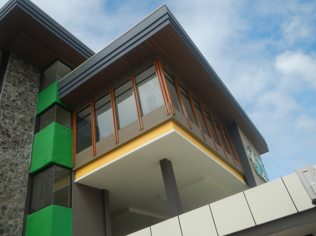 Moderne Häuser mit grüner und gelber Fassade, großen Glasfenstern und wolkenartigem Hintergrund.