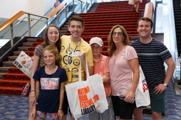 Eine Gruppe von Menschen, die vor einer Rolltreppe an der Nationalen Buchmesse 2019 lächeln und Taschen halten.