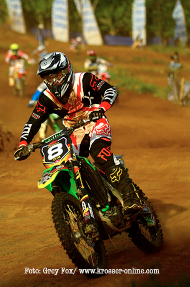 Mehrere Personen bei einer Motorrad-Rennerei, alle mit Helmen, mit Text am unteren Bildrand.