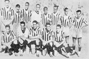 Ein Schwarz-Weiß-Foto einer Fußballmannschaft, mit einigen stehenden und anderen sitzenden Spielern und Text unten.