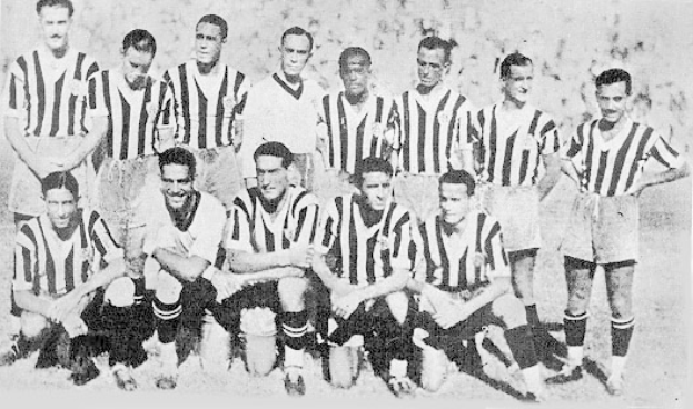 Ein Schwarz-Weiß-Foto einer Fußballmannschaft, mit einigen stehenden und anderen sitzenden Spielern und Text unten.