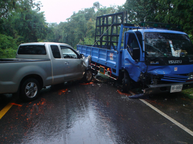 Ein schwerbeschädigter Lkw mit eingedellter Front und verbeulter Karosserie liegt auf der Seite einer Straße, umgeben von Bäumen unter einem klaren blauen Himmel.