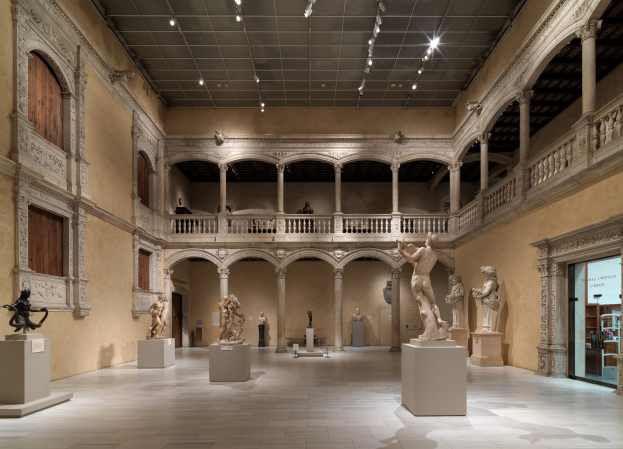 Große Museumsgalerie mit zahlreichen Statuen und Skulpturen auf Sockeln, architektonischen Elementen wie Säulen und Geländern, Deckenbeleuchtung und einigen Besuchern.