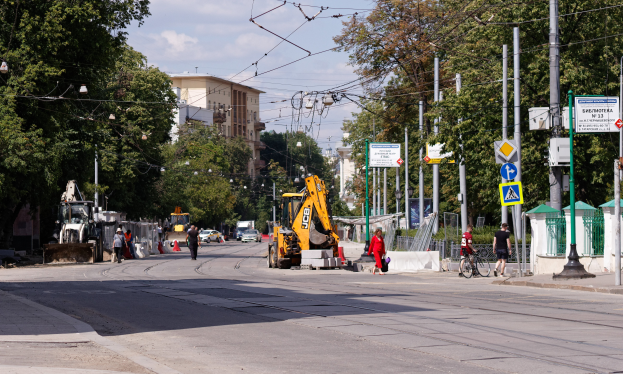 Eine Stadtstraße mit einer Baustelle, Fahrzeugen, Fußgängern, einem Radfahrer, Verkehrskegeln, Polen, Schildern, Strommasten mit Drähten, Bäumen, Gebäuden mit Fenstern und einem bewölkten Himmel.