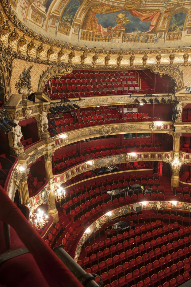 Ein prächtiger Innenraum der Royal Opera House in London mit Sitzreihen, verzierten Geländern, Säulen, Wandskulpturen, Deckenleuchten und einem großen Deckengemälde.