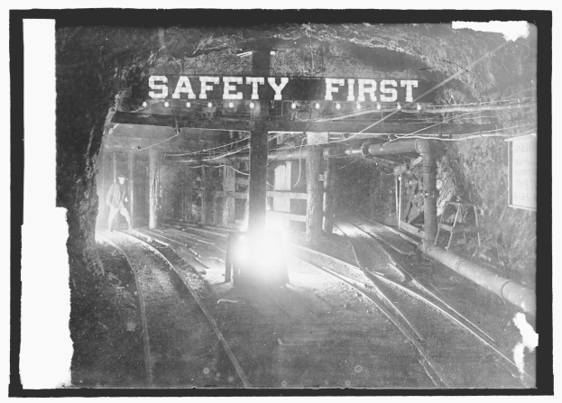 Schwarzes und weißes Foto eines Zuges, der durch einen Tunnel fährt, mit einer Person auf dem Bahnsteig im Vordergrund und Sicherheitshinweisen im Hintergrund.
