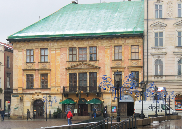 Ein großes Gebäude mit grüner Dachfläche in einer städtischen Umgebung mit Straßenlaternen, Laternen, Fahrzeugen, Fußgängern, Geländern, Bäumen und einem klaren Himmel.