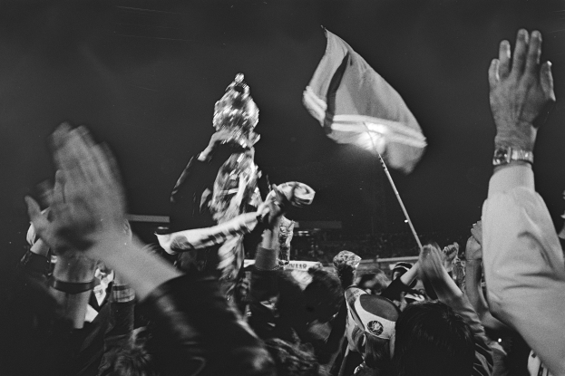 Schwarzes und weißes Foto einer Menge bei einem Konzert mit einigen Menschen, die ihre Hände heben und einer, der eine Flagge hält.