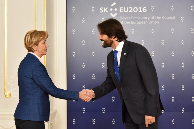 Bundeskanzlerin Angela Merkel und Bundespräsident Joachim Gauck schütteln sich lachend vor einer Wand mit einem 'EU-Gipfel'-Schild und einer Tür die Hände.