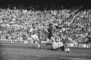 Schwarzes und weißes Foto von Männern, die auf einem Feld Fußball spielen, mit Zuschauern im Hintergrund und einem Banner mit der Aufschrift «Bundesliga 1978-79 Ajax 1-1 Hannover 96».