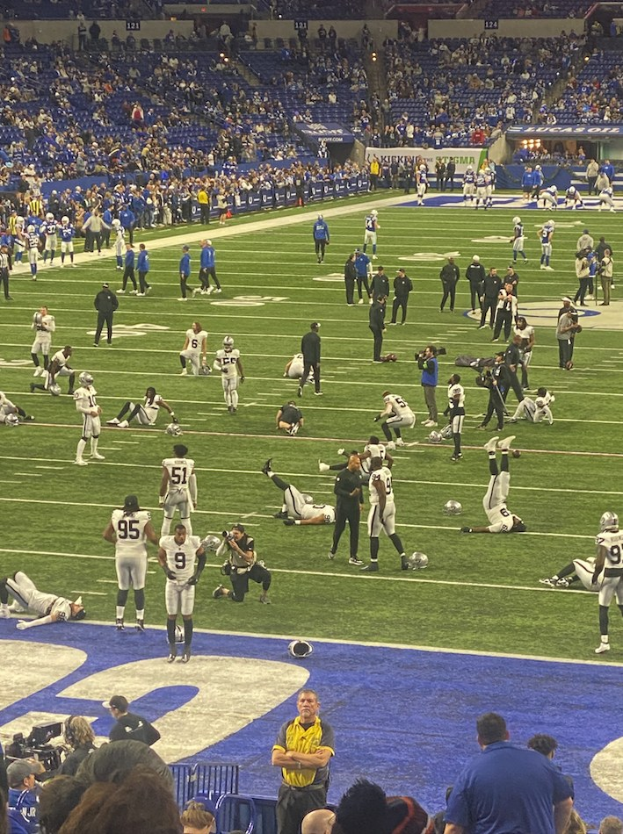 Ein Fußballspiel in einem Stadion mit Spielern auf dem Feld und Zuschauern im Hintergrund, einschließlich einer Person, die eine Kamera für die Live-Übertragung bedient.