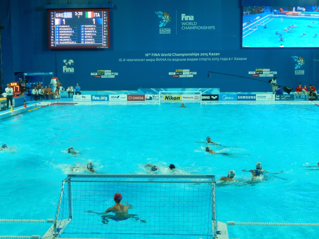 Gruppe von Athleten, die Wasserball in einem Pool bei den 2016 FINA-Weltmeisterschaften in Kazan spielen, mit einem Netz, das den Pool teilt, und Zuschauern auf der linken Seite.