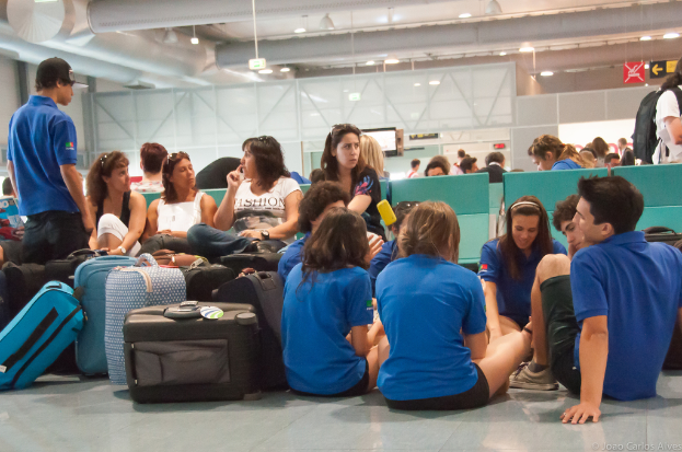 Ein belebter Flughafen mit vielen Wartenden auf Flüge, Gepäck auf der linken Seite und Glasdoors mit Richtungsschildern im Hintergrund.