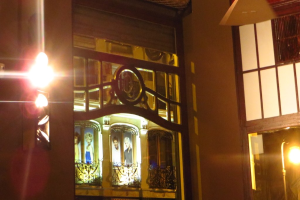 Gebäudefassade mit Metallgrills, Plakaten und Außenleuchten.