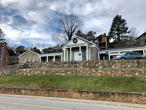 Steinwand mit parkenden Autos, angrenzende Gebäude mit Fenstern und Türen, Bäume und ein bewölkter Himmel, als das kürzlich wiedereröffnete Weltkulturerbe-Museum bezeichnet.