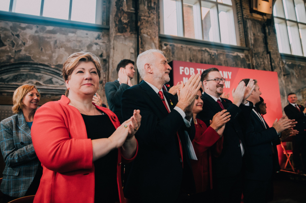Eine Gruppe von Menschen, die vor einer Menge klatschen, mit einem Banner im Hintergrund, das einen Wahlsieg anzeigt.