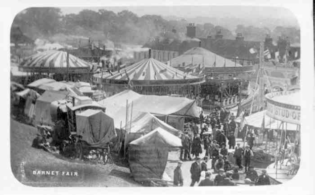 Schwarzes und weißes Foto eines Volksfests mit Zelten, Menschen, Wagen, Pfählen, Bäumen und Gebäuden, beschriftet mit "Barnet Fair, London, England" unten.