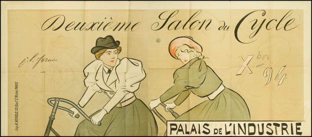 Zwei Frauen in farbenfrohen Kleidern fahren Fahrräder in einem Salon, sie lächeln und ein Plakat ist im Hintergrund zu sehen.