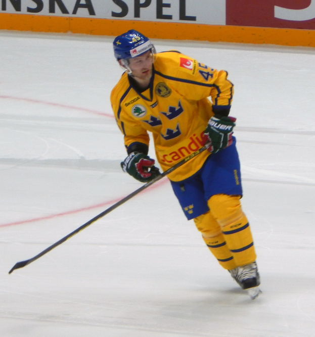 Eishockeyspieler in Bewegung auf dem Eis mit Helm, Handschuhen und Schlittschuhen, der einen Hockeystock hält, mit einer textgefüllten Tafel im Hintergrund.