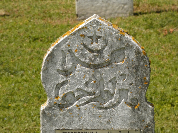 Grabstein mit arabischer Schrift in einem grasbewachsenen Friedhof.