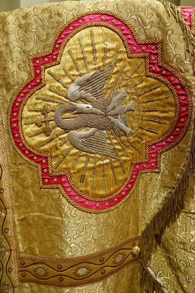 Nahaufnahme eines Priestergewandes mit aufwendiger Gold- und Rotstickerei und luxuriösem, königlich anmutendem Design vor einer Wand im Hintergrund.