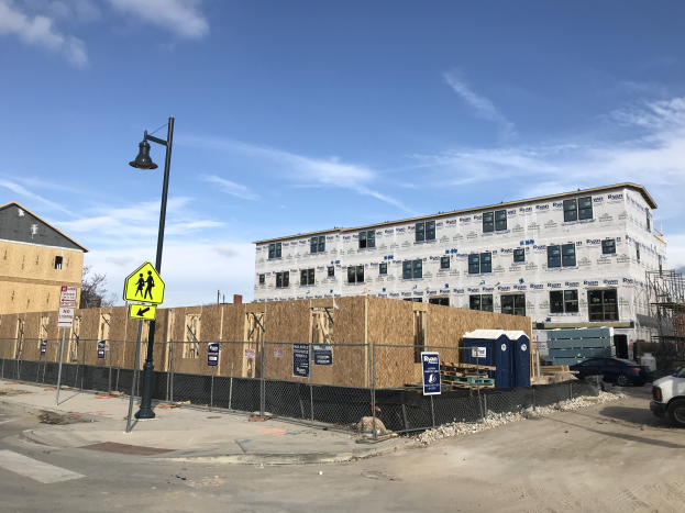 Gro├če Baustelle an einer Straßenecke, umgeben von Baustoffen, mit Bäumen und bewölktem Himmel im Hintergrund.