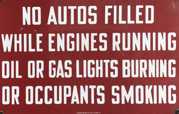 Rotes Schild mit weißer Schrift, das davor warnt, Autos aufzufüllen, während die Motoren laufen, Öl- oder Gaslampen brennen oder Insassen rauchen.