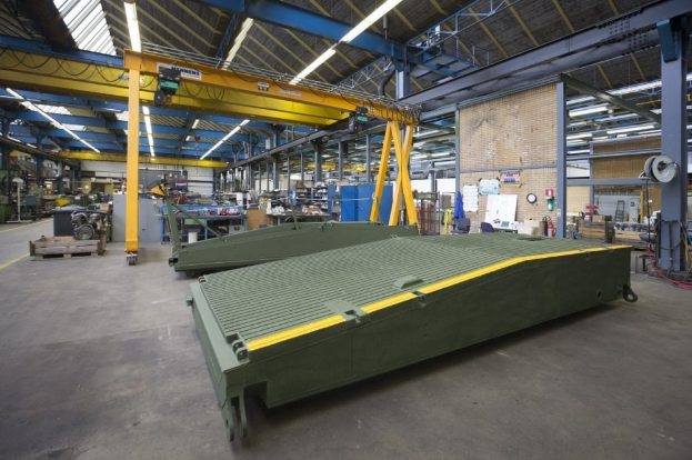 Ein großes Lagerhaus mit grünen Containern, Maschinen, Polen, Lampen, Stangen und anderen Gegenständen, mit einer Uhr und Papieren an einer Wand im Hintergrund.