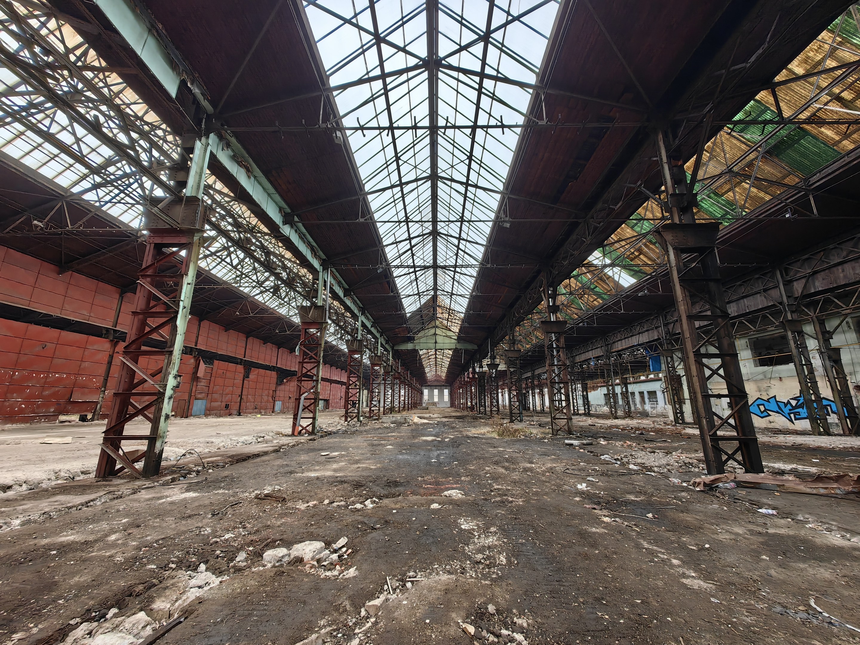 Verlassene Gebäude mit verstreuter Trümmern, Metallstangen, einer beschädigten Glasdecke, graffiti-bedeckten Wänden und zerbrochenen Fenstern.